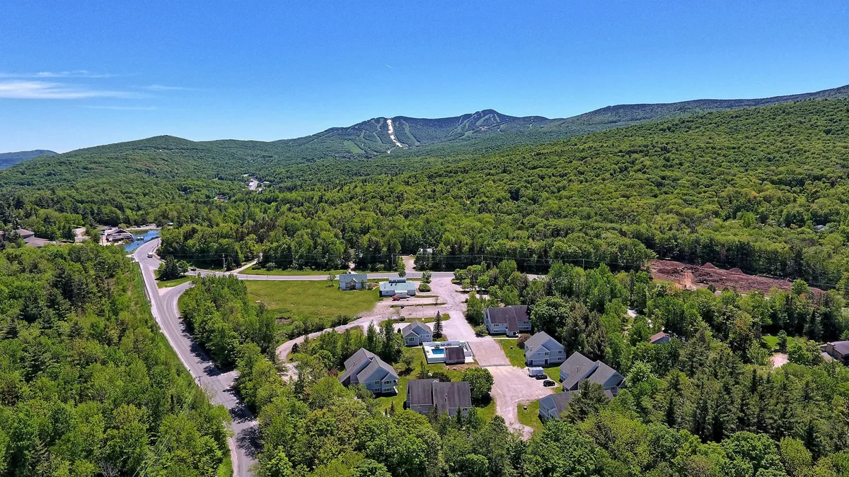 A sweeping view of snow-capped mountains overlooking a residential area with a winding road. The landscape evokes the atmosphere of an alpine getaway, capturing the proximity to nature and adventure. The scene is serene, yet hints at the excitement of outdoor activities just beyond the doorstep.