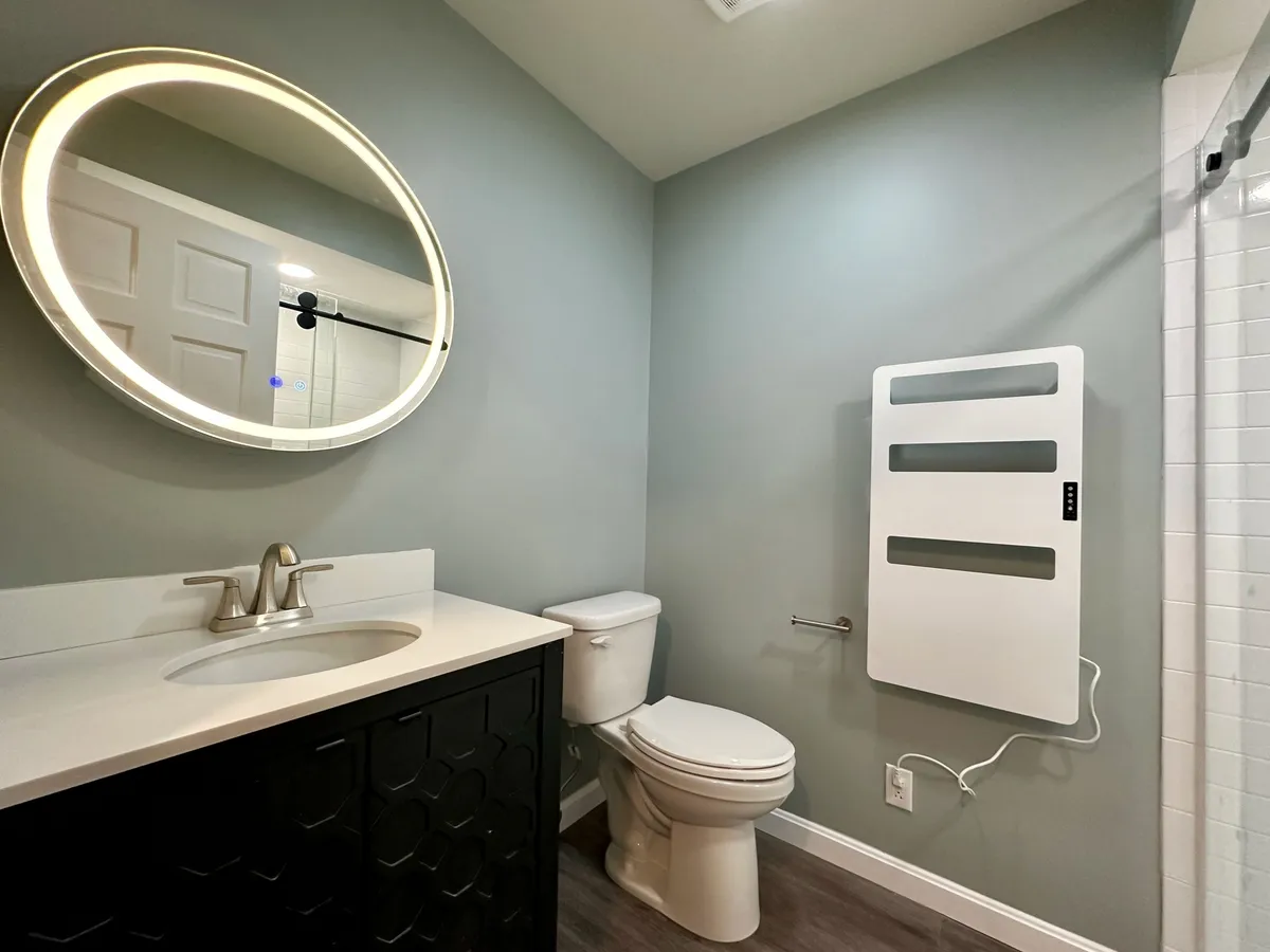 A stylish bathroom scene with a glowing round mirror, modern vanity, and towel warmer creates a calming, spa-like atmosphere—ideal for self-care and unwinding.