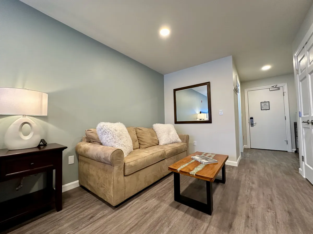 A comfortable living area with a plush sofa, a coffee table, a warm lamp, and a decorative mirror. The scene sets an inviting mood for socializing or sharing moments over coffee before heading out or after returning from local hotspots.