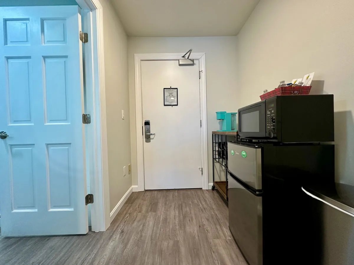 A view of the practical kitchenette area includes a mini fridge, microwave, and welcoming entrance door. The setup is compact and functional, perfect for preparing snacks, making coffee, or enjoying a quick meal before a day of activities.