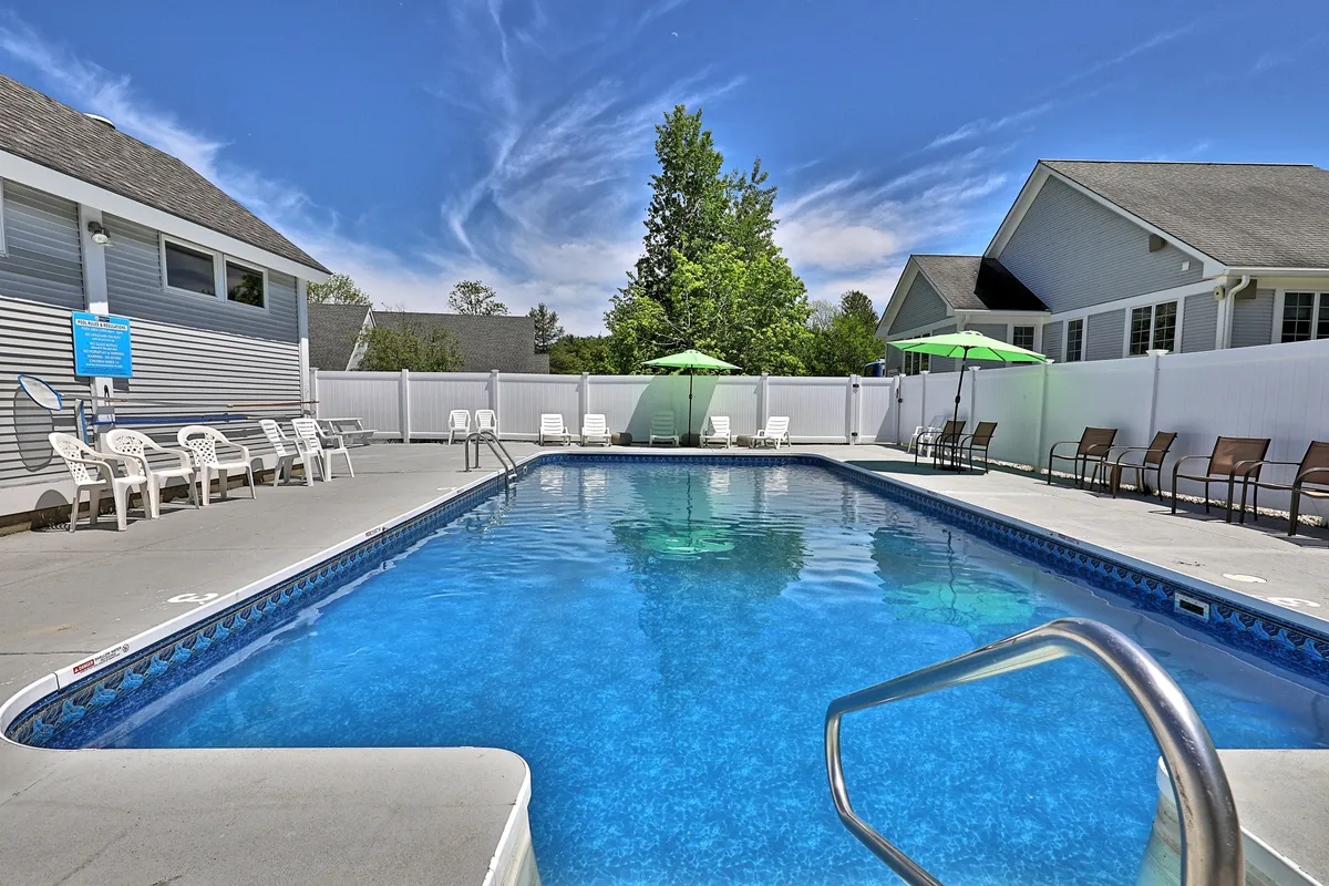 The image captures a gleaming outdoor swimming pool surrounded by comfortable lounge chairs and large umbrellas. The pool area is set against an open sky, suggesting ample sunshine for summer relaxation. The seating invites guests to sunbathe, read, or socialize poolside, while the clear water looks perfect for a refreshing swim after a hike or day out.
